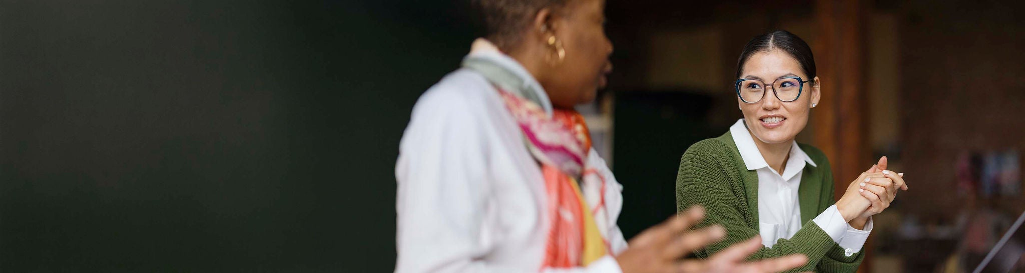 A professional woman in smart casual attire collaborates with a colleague using a laptop in a modern office. She is focused and attentive, fostering a productive work environment.