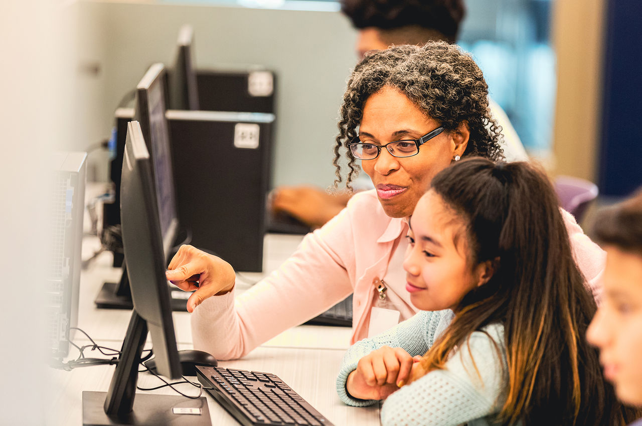 Woman in a computer classroom teaching a young girl. 