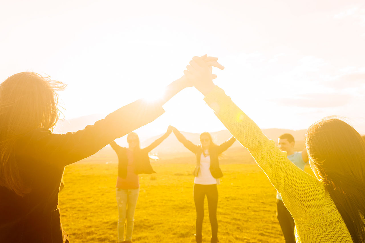 Circle of people joining hands in a field. 