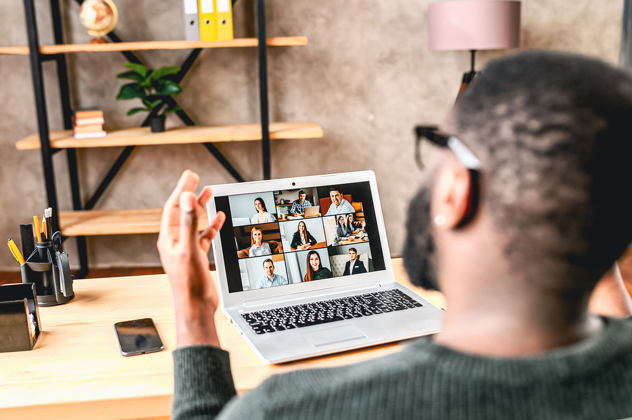 A man videoconferencing with colleagues from his home office.