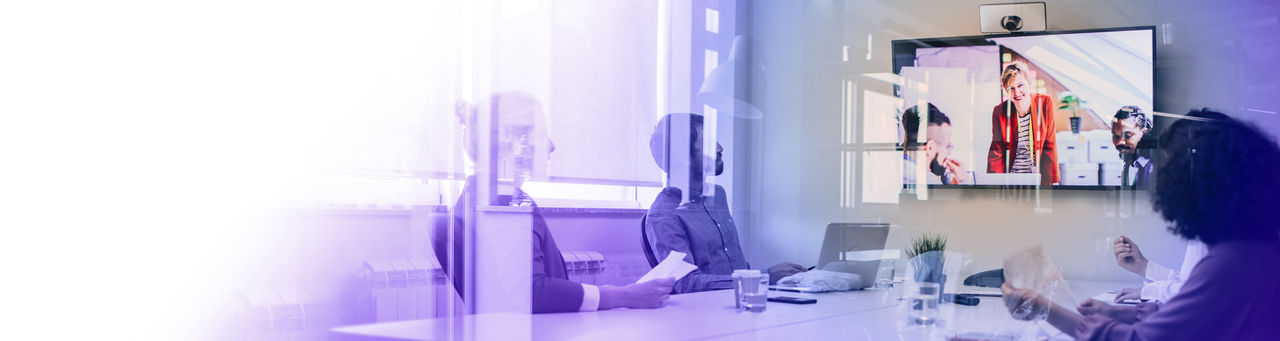 Executives at a conference table speaking to colleages on a videoconference screen.