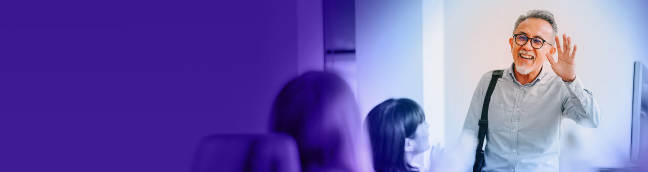 Smiling man greeting colleagues as he enters a conference room.