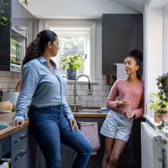 Happy mother and daughter bonding at home in the kitchen and talking - family concepts